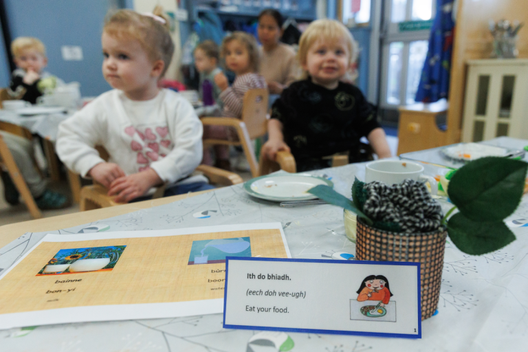 Children in an early years group behind a table with Gaelic learning materials.