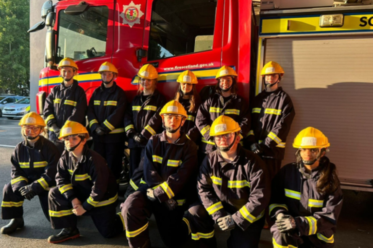 Pupils in fire fighter equipment in front of a fire engine