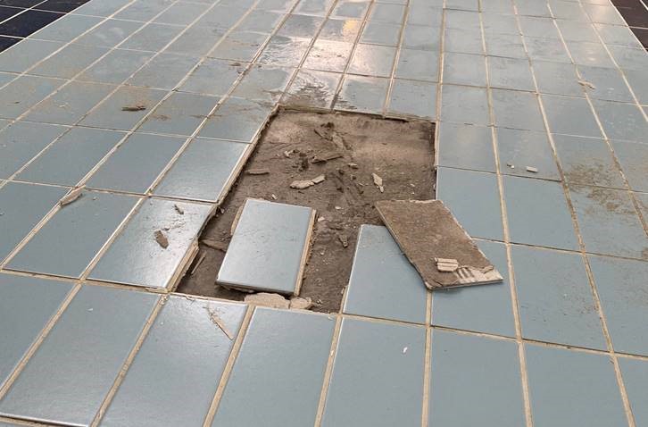 A tile floor showing missing tiles and exposed loose cement underneath